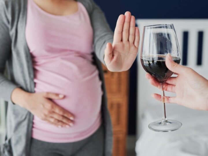 Kobieta w ciąży głaszcząca swój brzuch odmawia kieliszka wina.